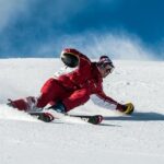 A skier in vibrant red gear skillfully navigates a snowy slope on a sunny day.